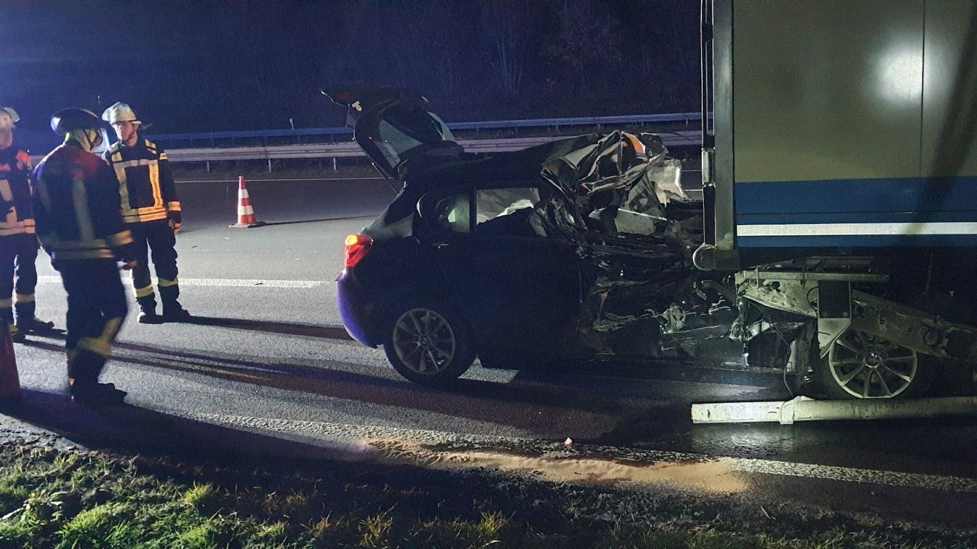 Der PKW klemmt unter dem LKW. An der Seite stehen Einsatzkräfte der Feuerwehr.