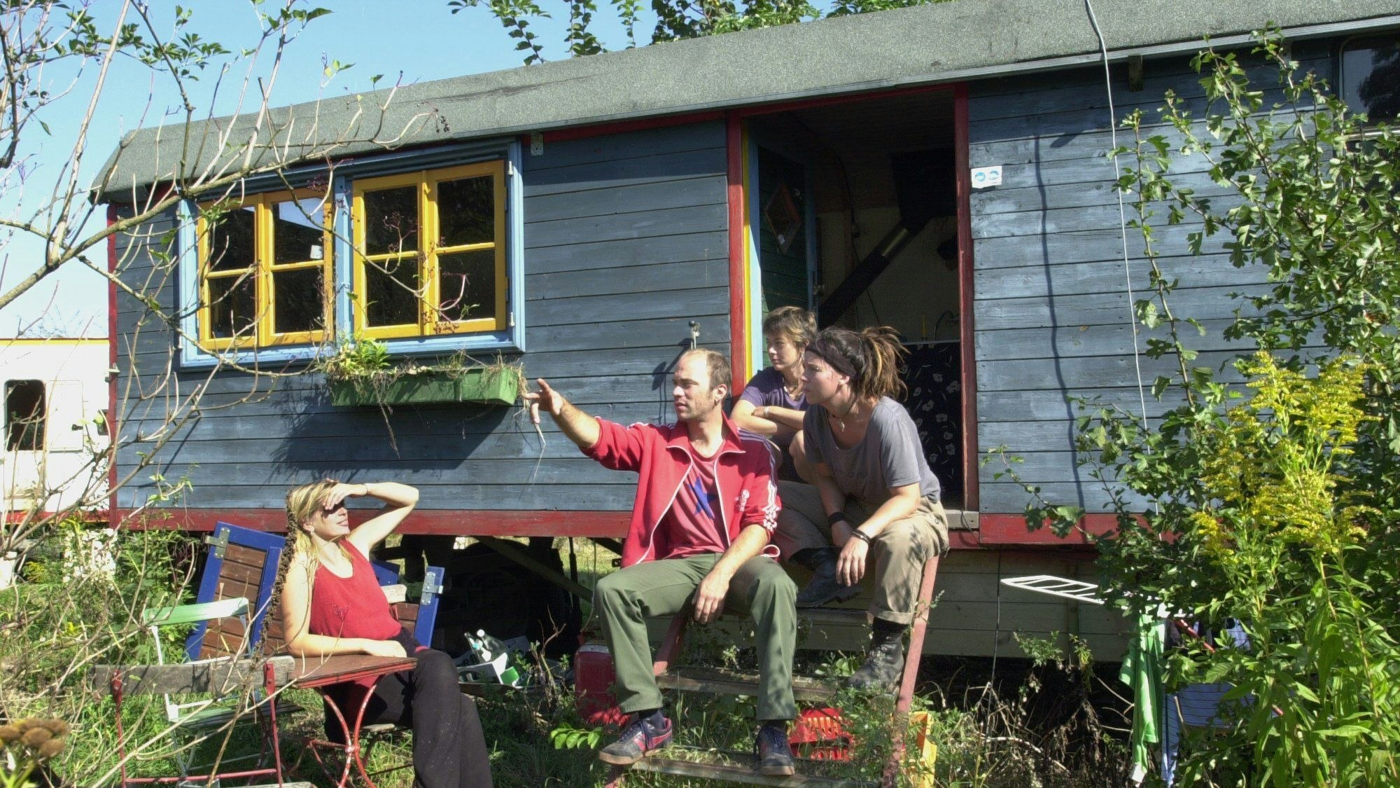 Bewohner des Kasseler Bauwagenplatzes sitzen vor einem Wagen in der Sonne.