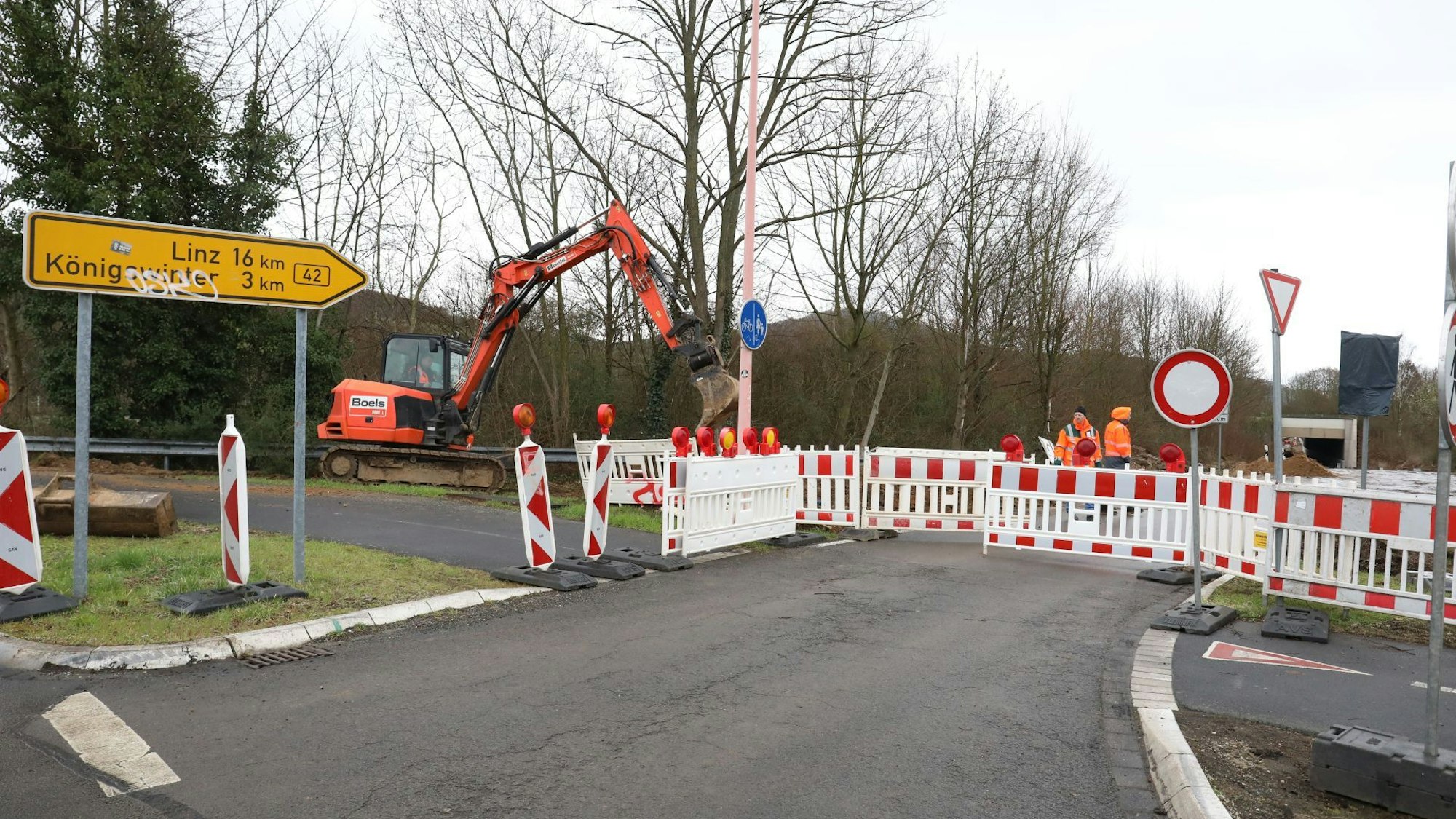 Weiß-rote Absperrbaken blockieren die Auffahrt Oberdollendorf zur B 42. Links am Rand bereitet ein Bagger Erdarbeiten für die Installation einer dynamischen Beschilderung vor.