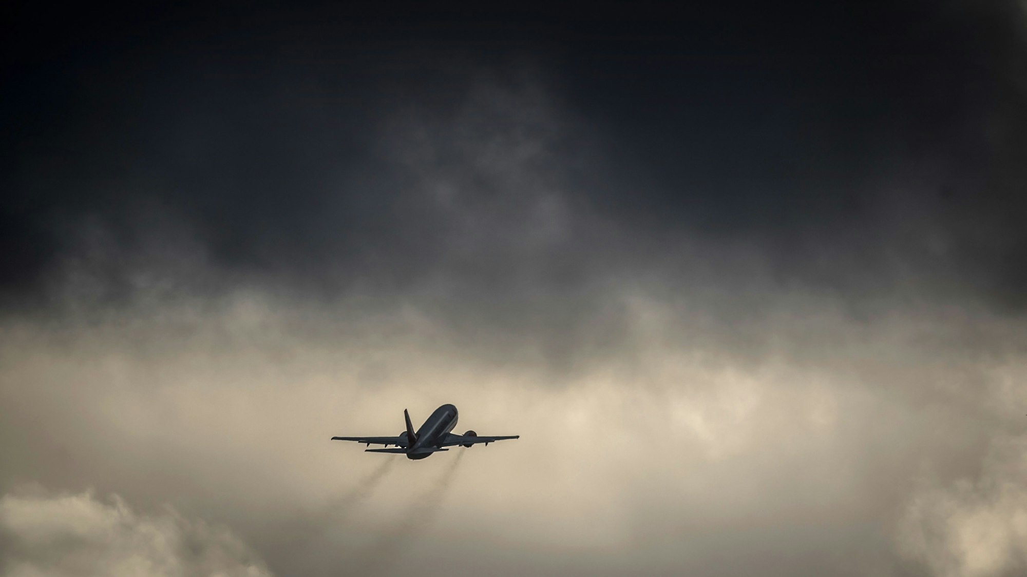 Ein Flugzeug fliegt nach dem Start auf eine dunkle Wolkenfront zu. (Symbolbild)