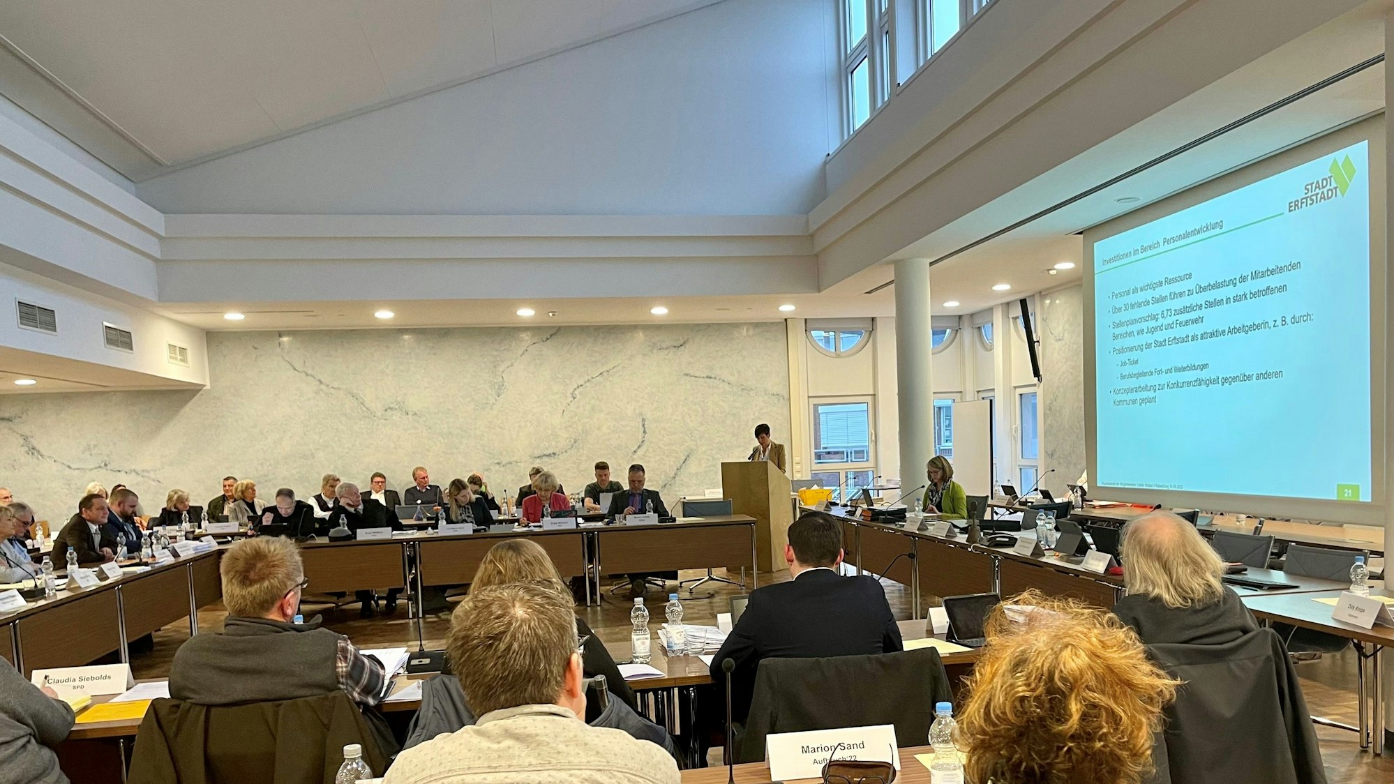 In einem gefüllten Saal hält Bürgermeisterin Carolin Weitzel eine PowerPoint-Präsentation.