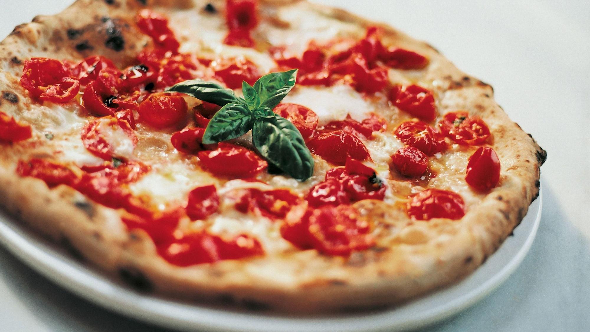 Das Symbolbild zeigt eine mit Tomaten und Basilikum belegte Pizza.