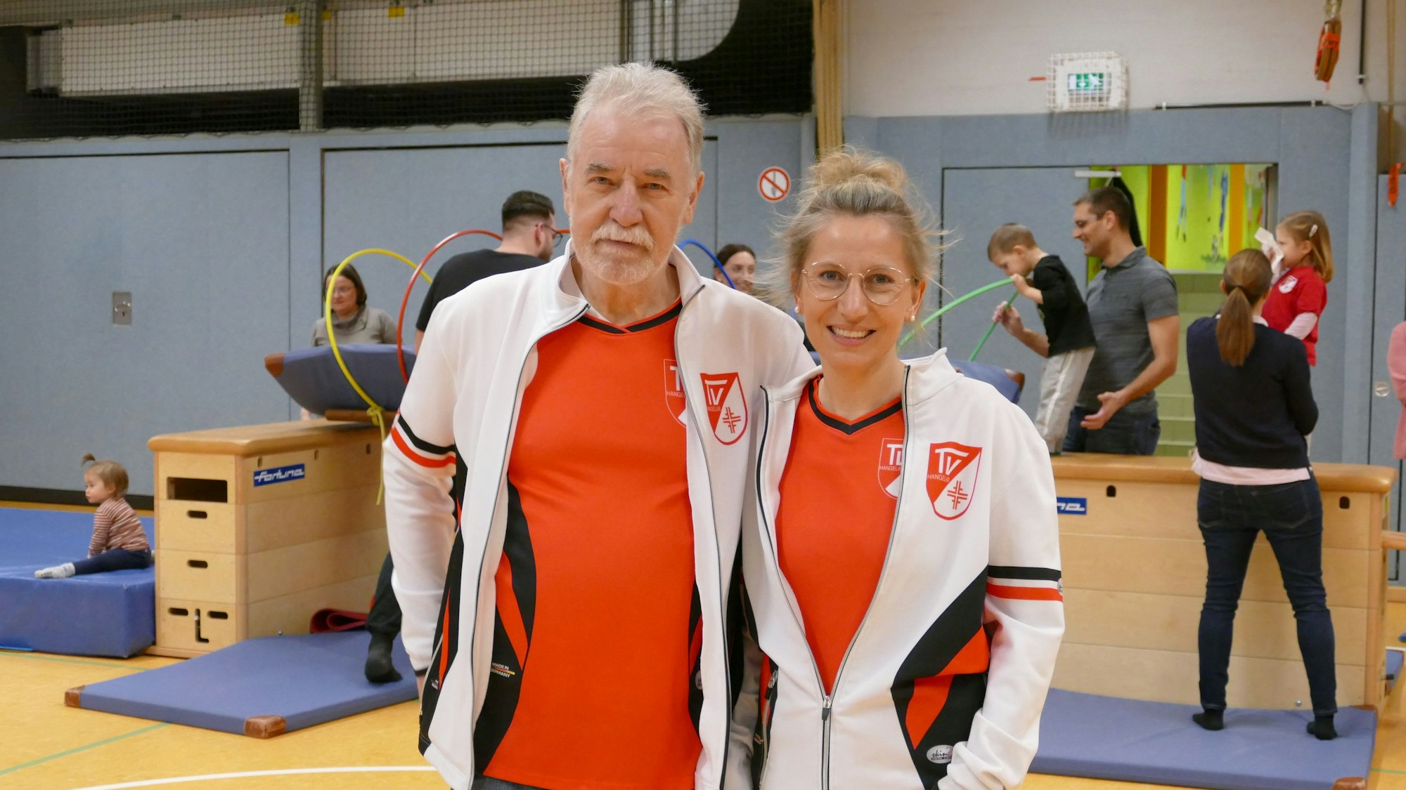 Eine Frau und ein Mann stehen in einer Sporthalle.