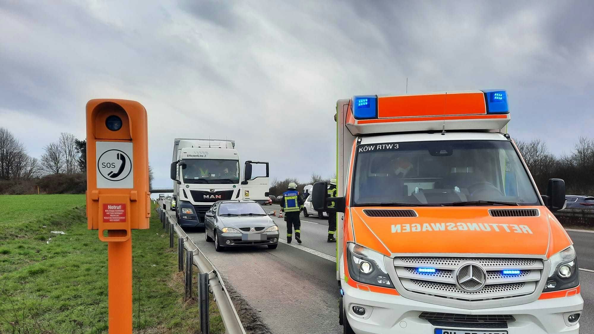Neben einer Notrufsäule steht ein Rettungswagen auf dem Seitenstreifen der Autobahn, dahinter die am Unfall beteiligten Fahrzeuge, ein Pkw und ein Lkw.