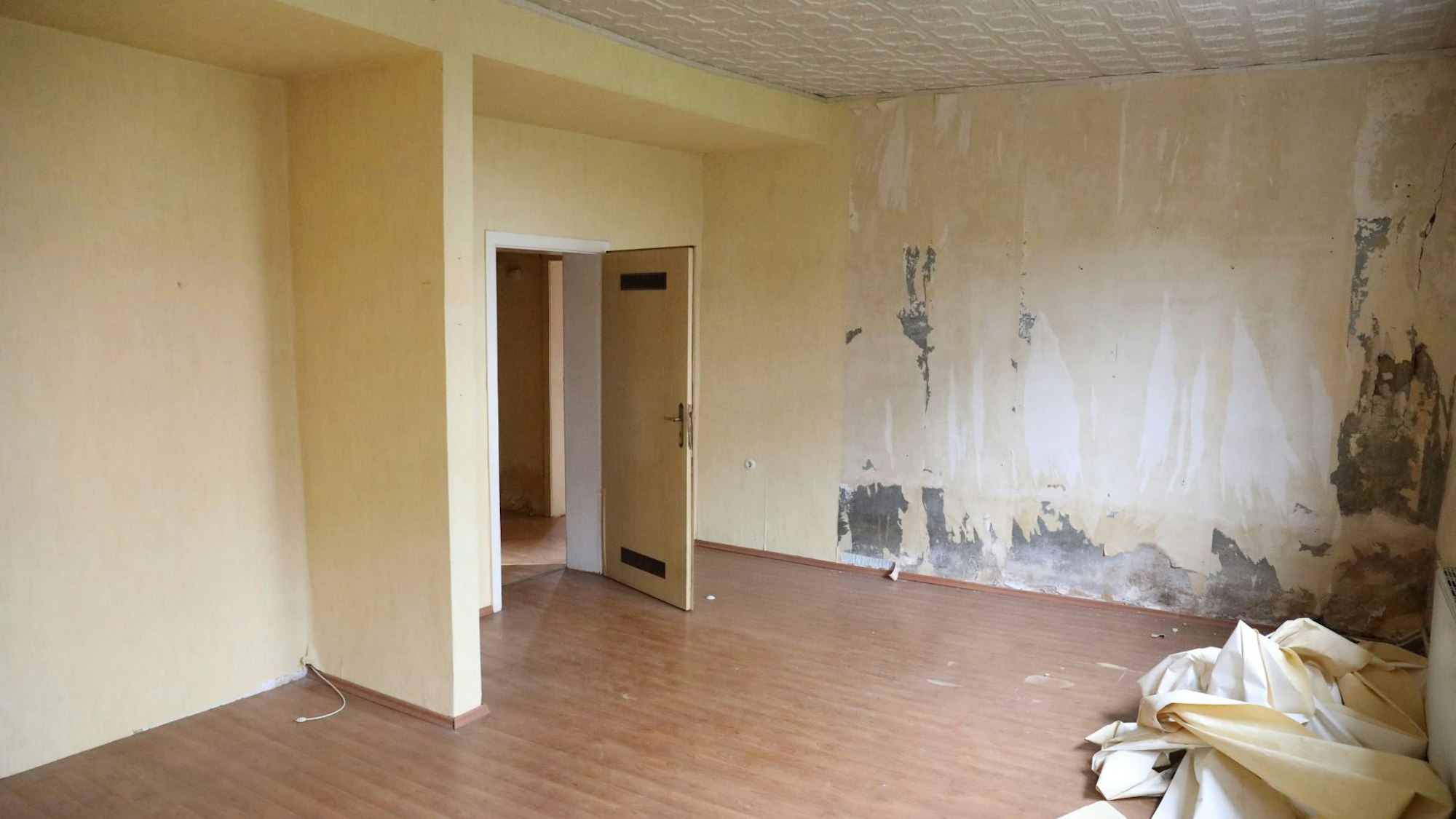 In einem leeren Raum mit gelben Wänden liegen abgerissene Tapeten auf dem Boden.