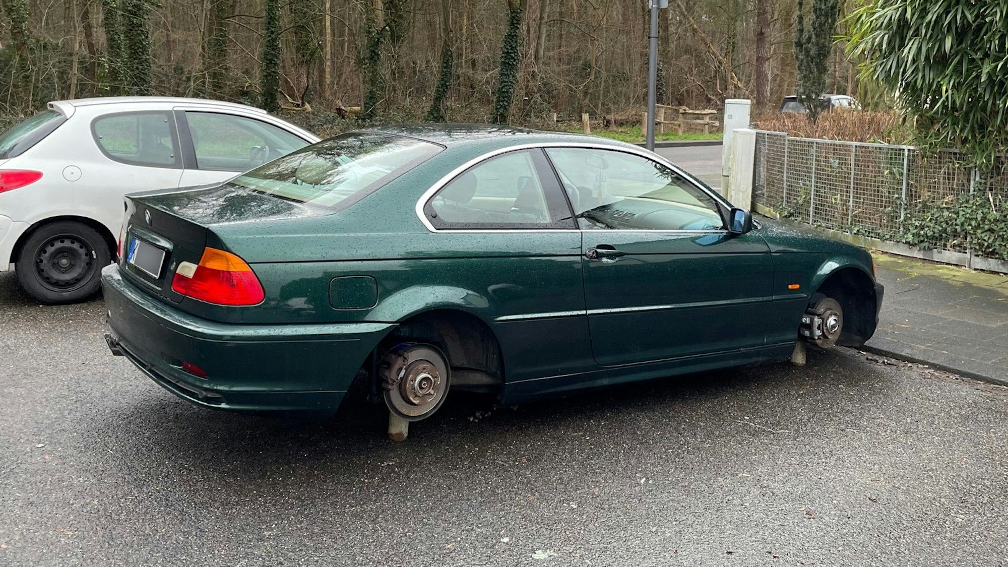 Ein schwarzer BMW steht mit demontierten Rädern auf Holzklötzen auf einem Parkplatz an der Straße „Am Klausenberg“ in Köln-Brück.