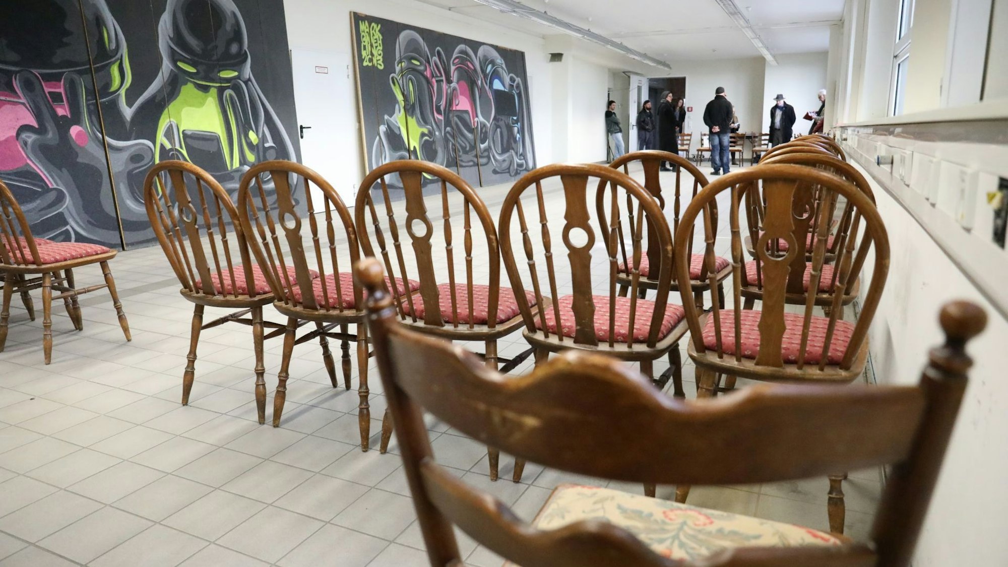 Im Vordergrund stehen in der ehemaligen Fabrikhalle braune Stühle, links an der Wand lehnen großformatige Streetart-Kunstwerke.