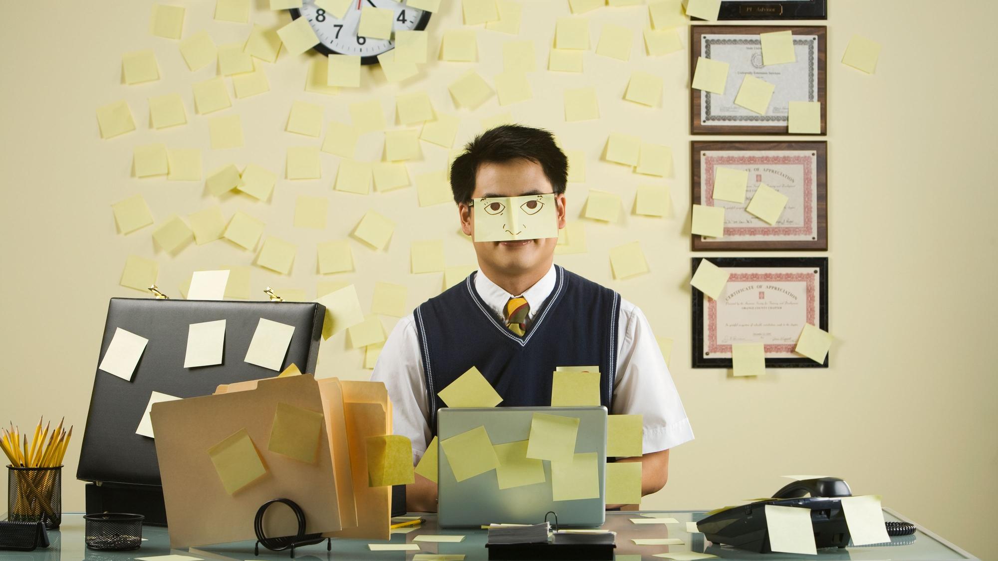 Ein Mann sitzt an einem Schreibtisch, dass mit Post-Its übersät ist.