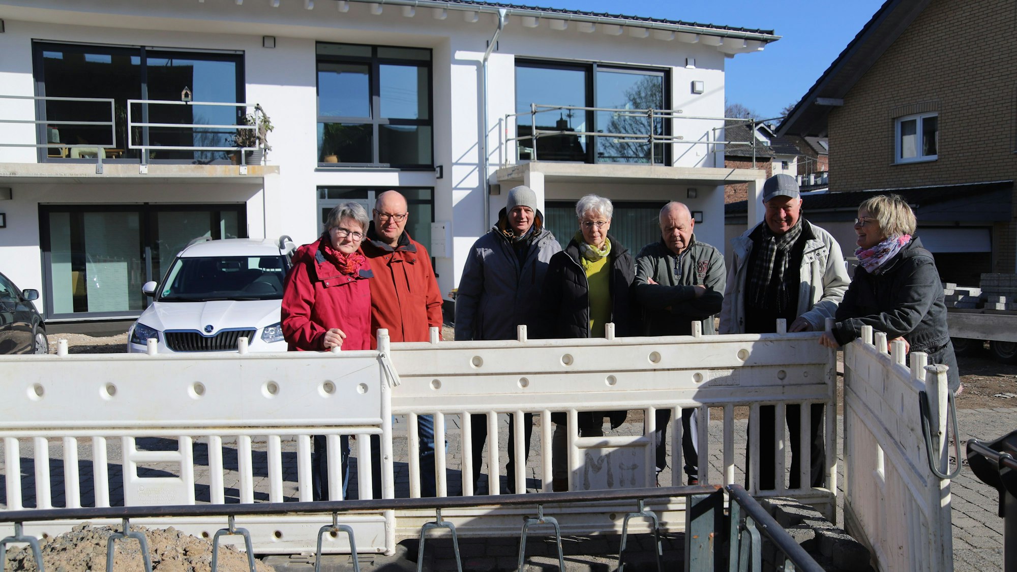 Mehrere Menschen stehen vor einem Mehrfamilienhaus. Vor ihnen befindet sich eine Baustelle.