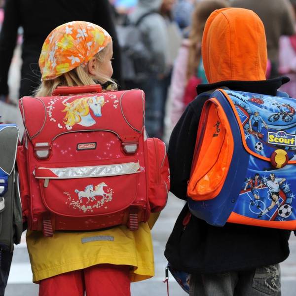Drei Kinder laufen mit ihren Schulranzen zur Schule.