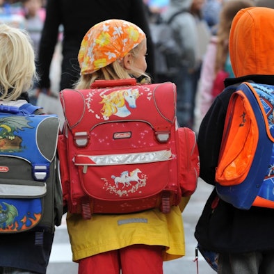 Drei Kinder laufen mit ihren Schulranzen zur Schule.