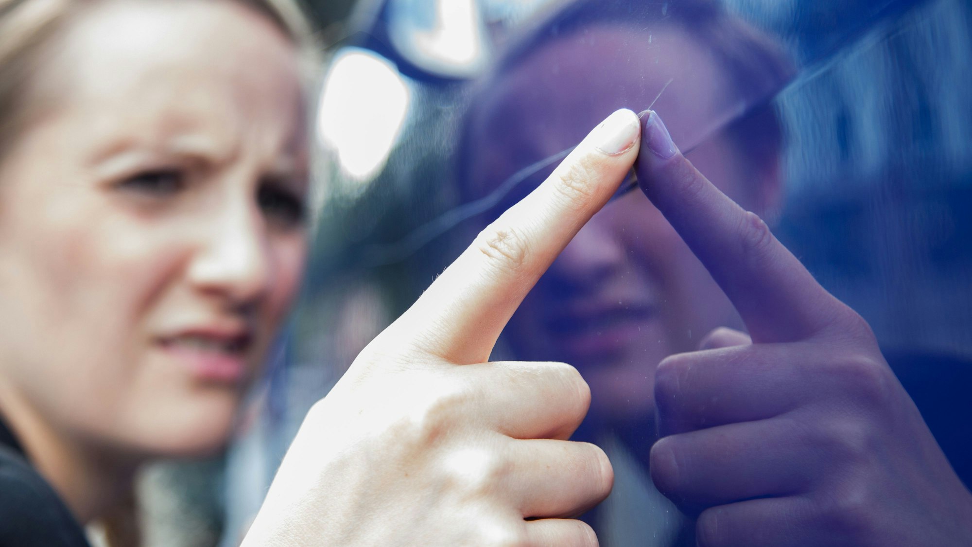 Eine Frau begutachtet an einen langen Kratzer im Lacke eines blauen Autos.