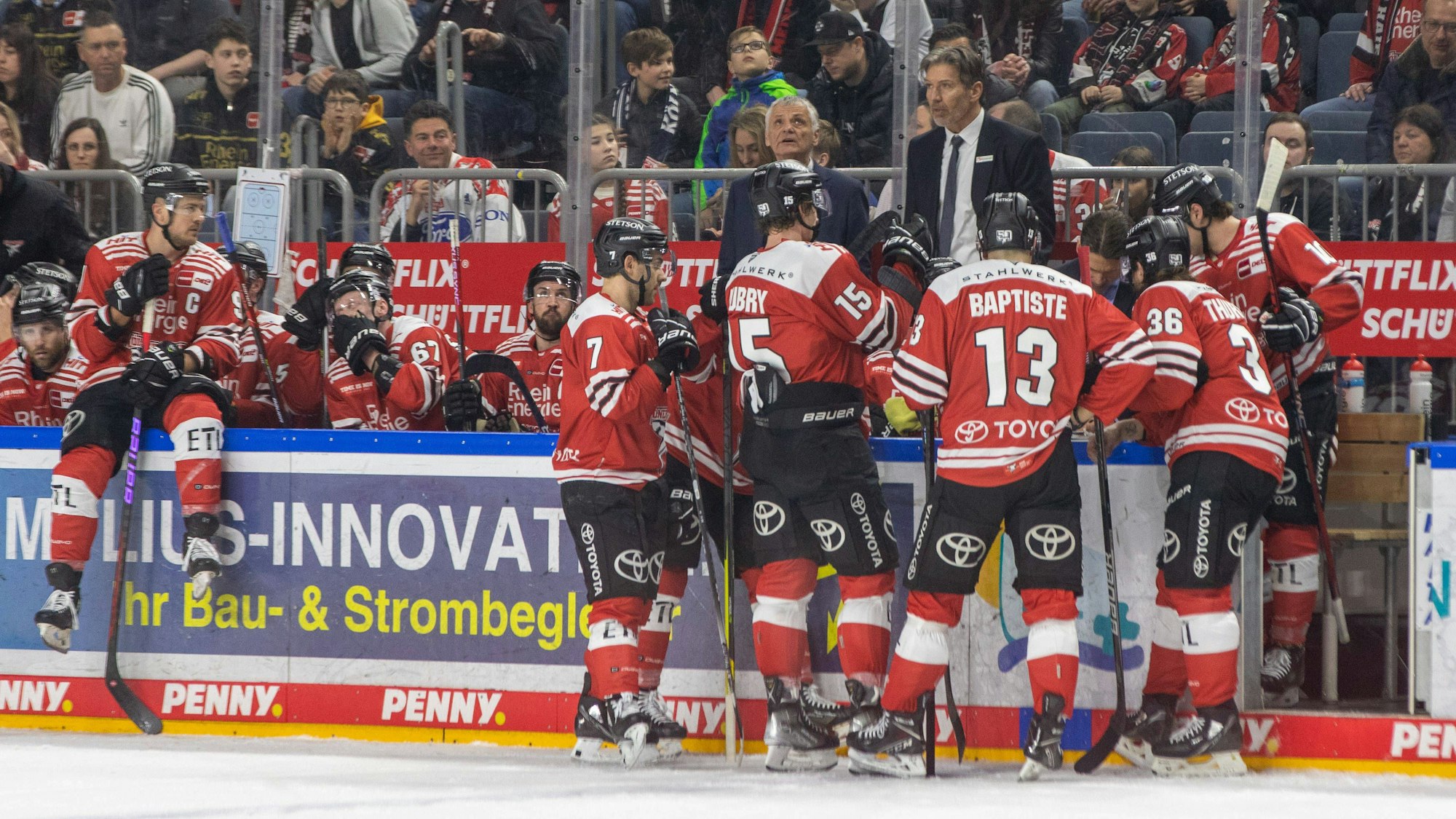 Spieler der Kölner Haie stehen an der Bande und erhalten Anweisungen von Trainer Uwe Krupp.