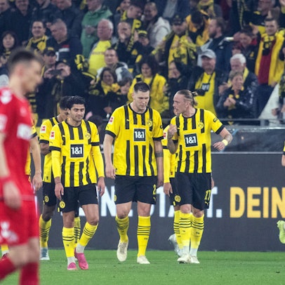 Spieler des BVB laufen auf das Spielfeld. Ein FC-SPieler ist unscharf abgebildet.