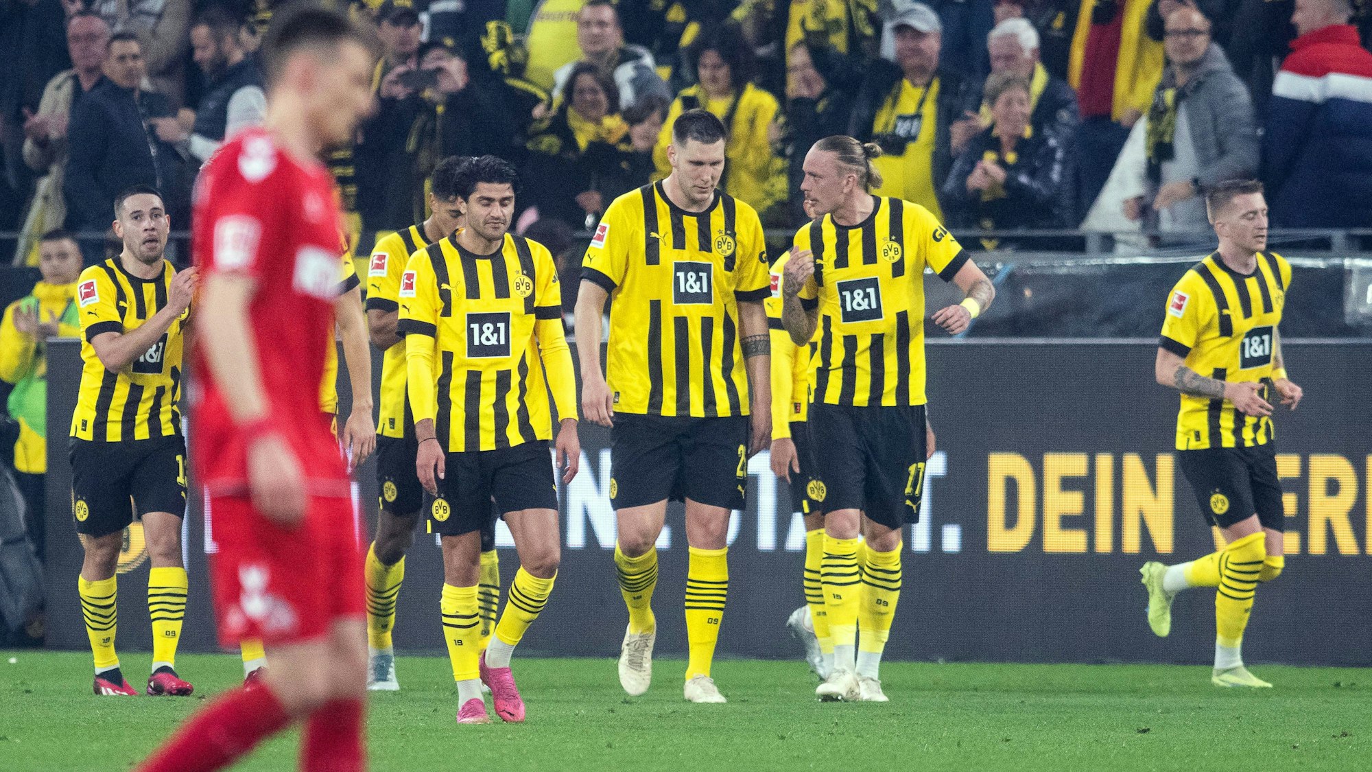 Spieler des BVB laufen auf das Spielfeld. Ein FC-SPieler ist unscharf abgebildet.
