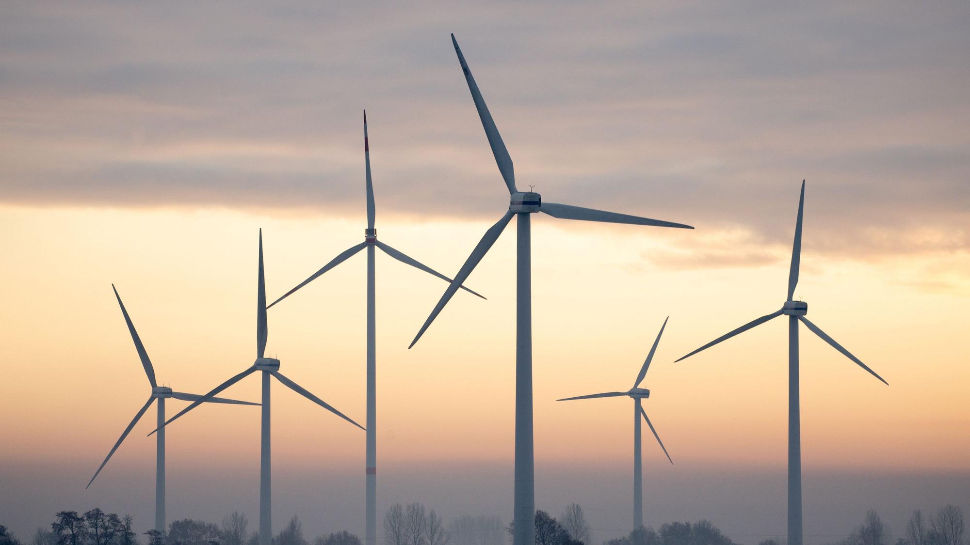 Windräder sind am rötlichen Himmel zu sehen.