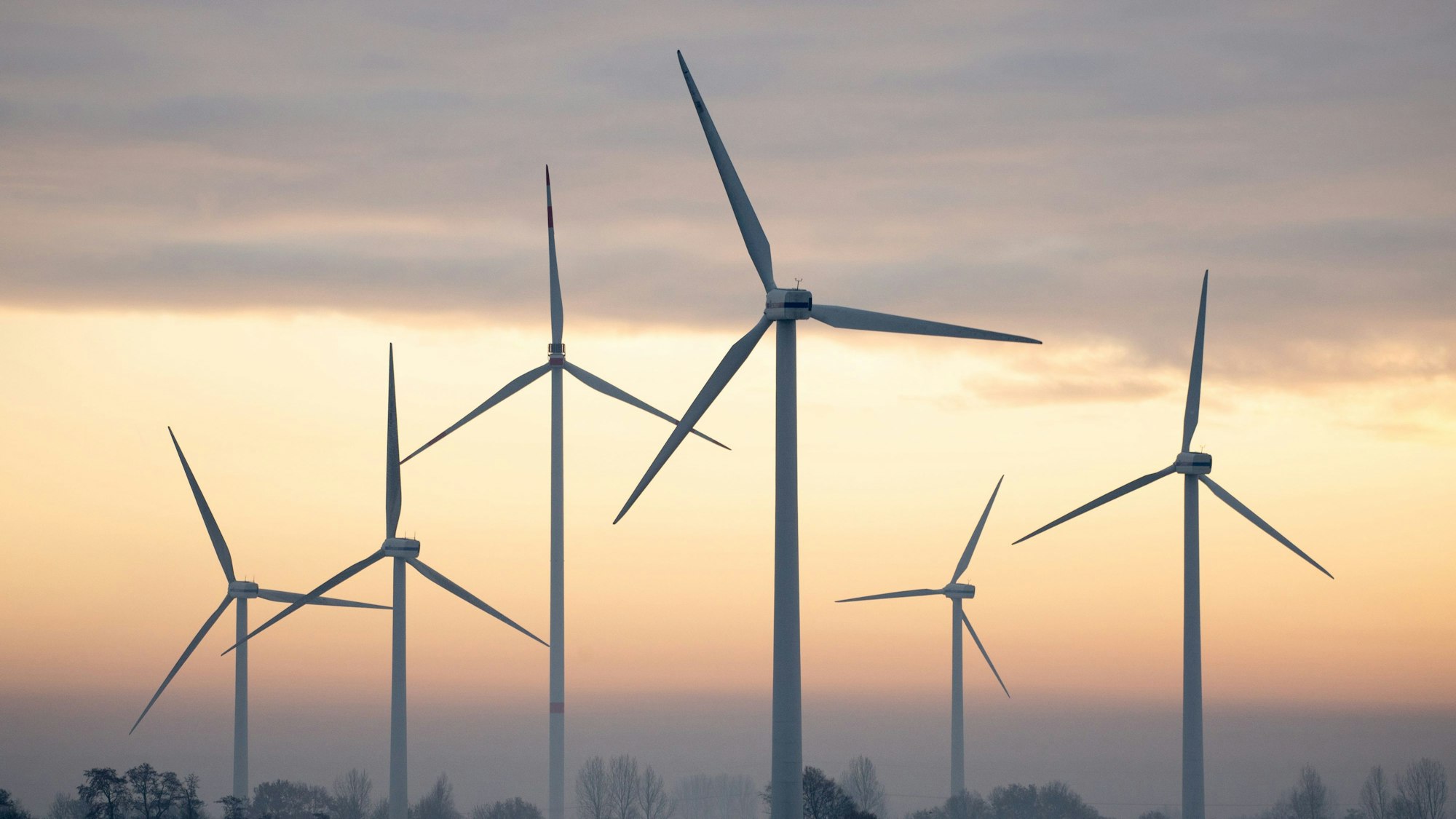 Windräder sind am rötlichen Himmel zu sehen.
