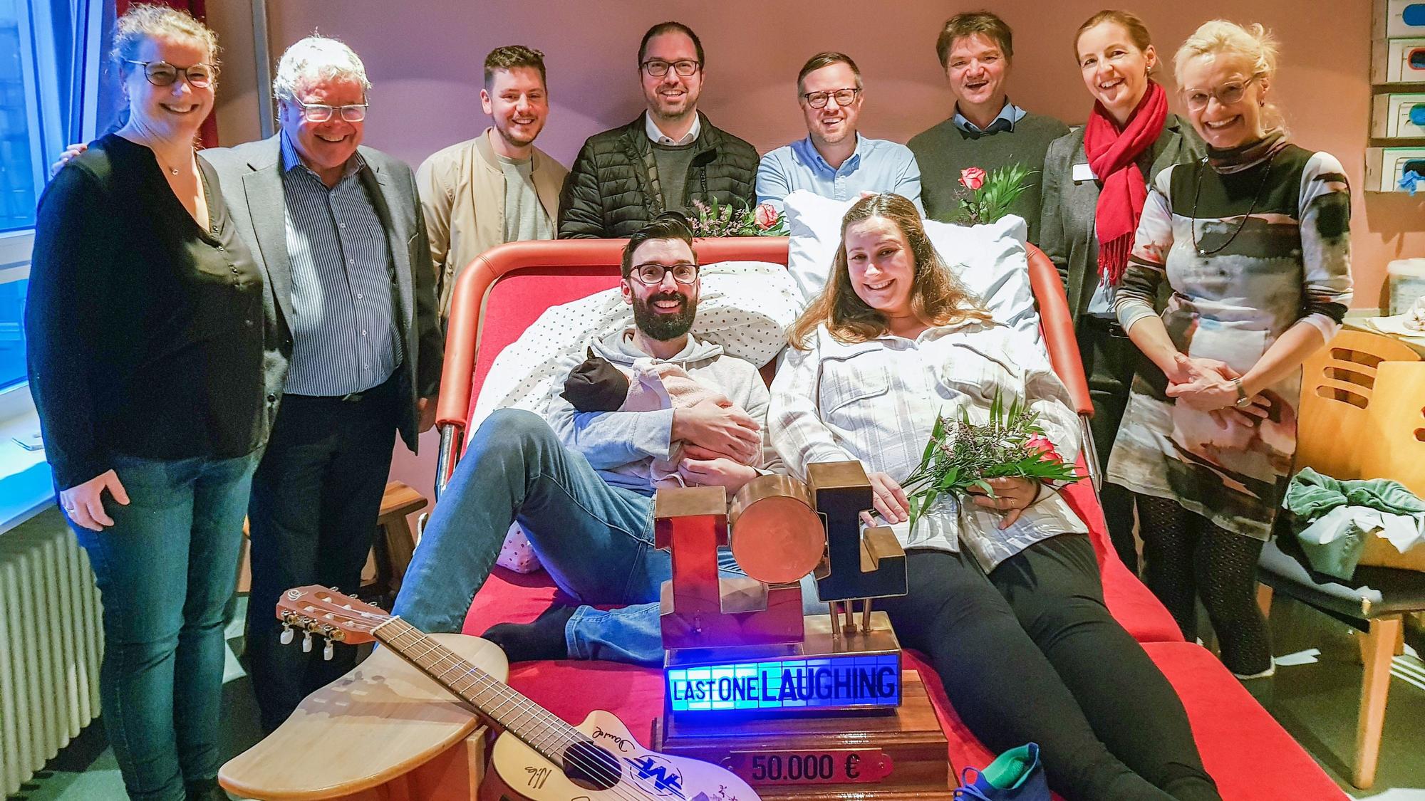 Viele Menschen stehen um das breite und moderne Kreißbett herum, ein Paar liegt drauf.