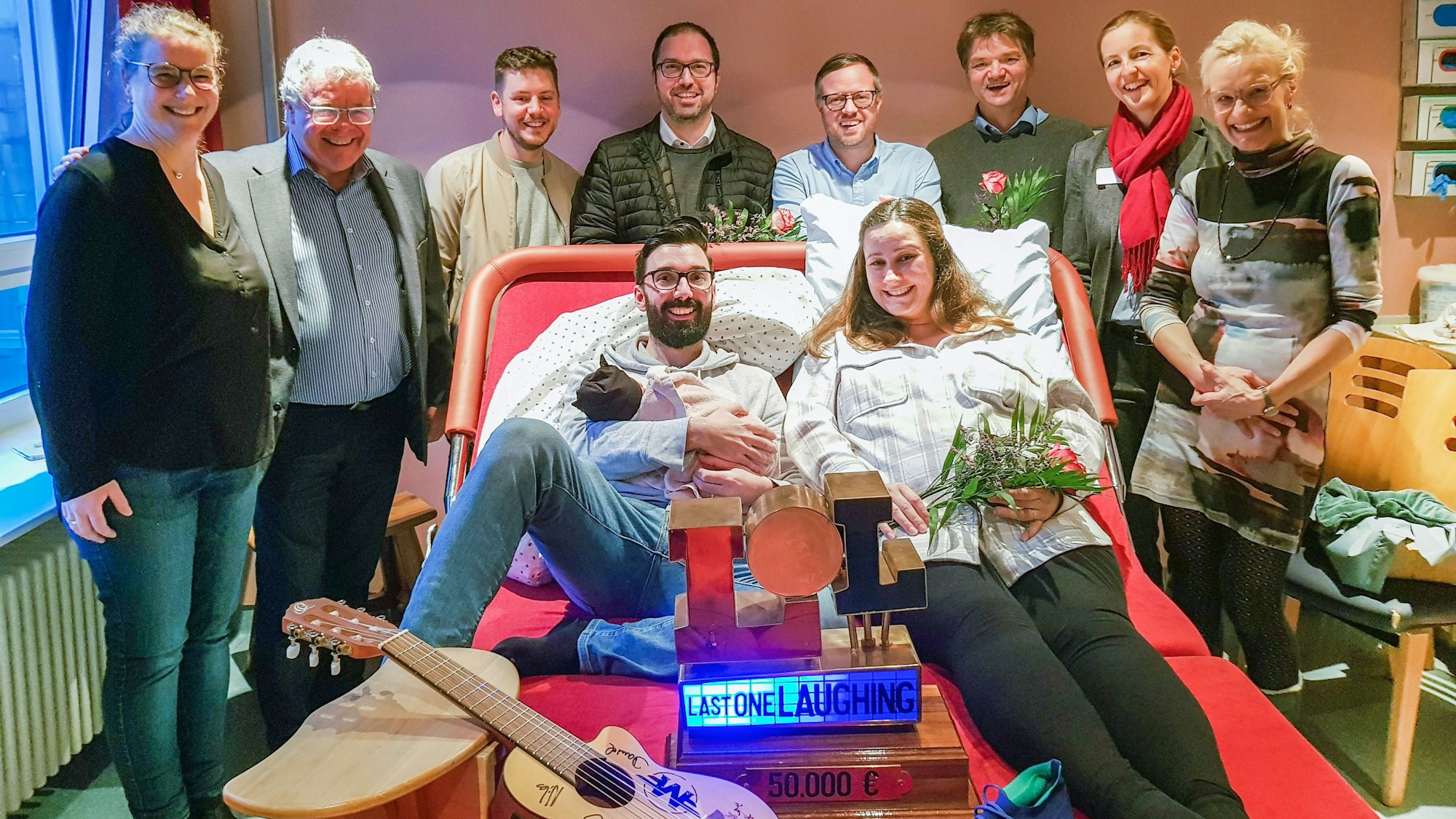 Viele Menschen stehen um das breite und moderne Kreißbett herum, ein Paar liegt drauf.