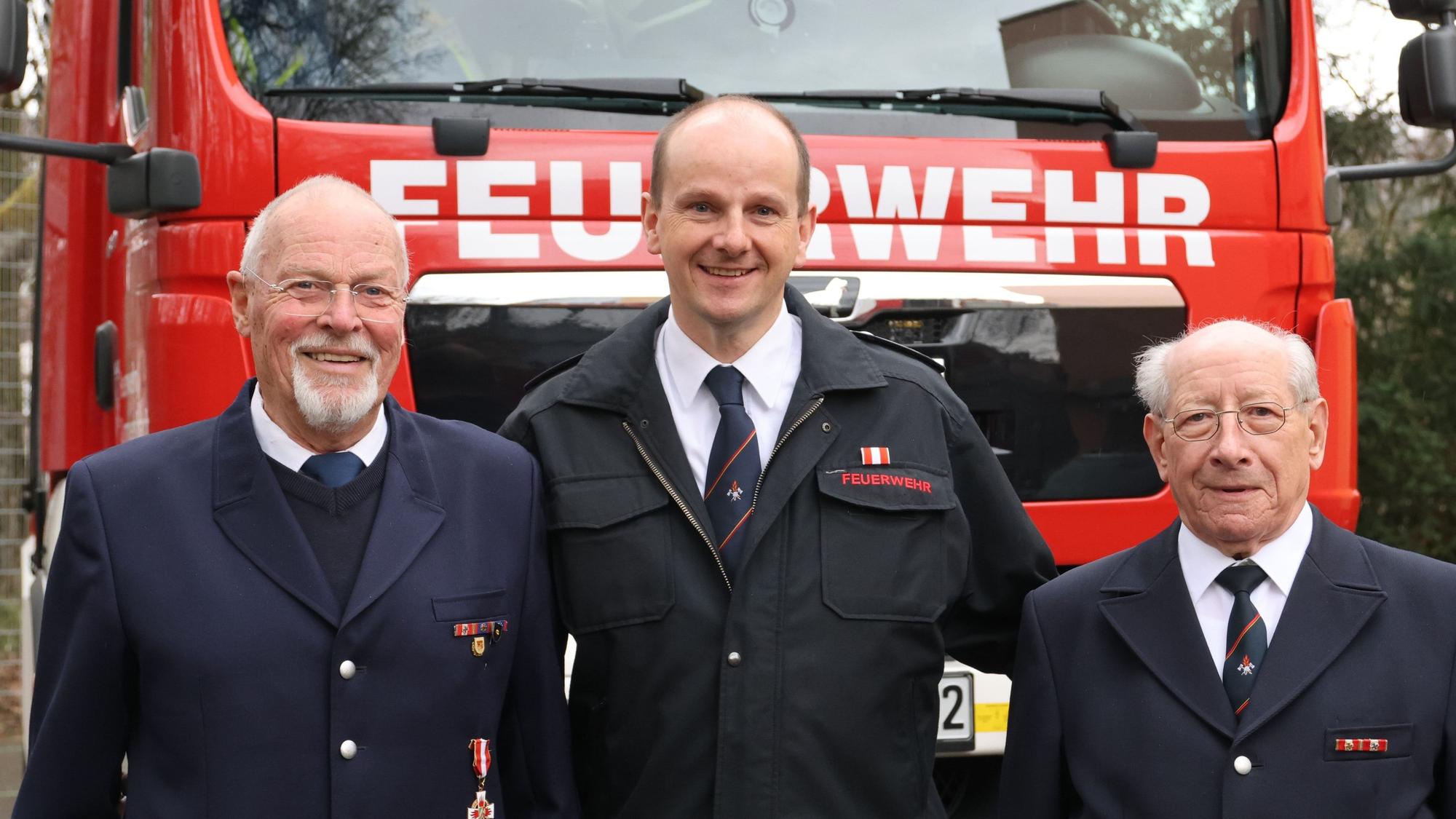 Drei Feuerwehrmänner stehen vor einem Feuerwehrwagen.