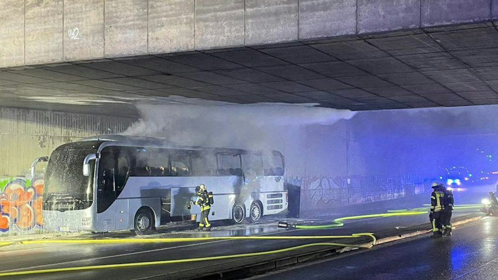 Ein Reisebus steht unter einer Brücke. Qualm steigt aus dem Bus auf.