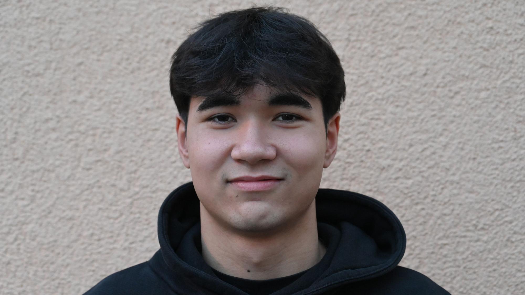 Franz Dolg trägt einen schwarzen Kapuzenpullober und lächelt in die Kamera