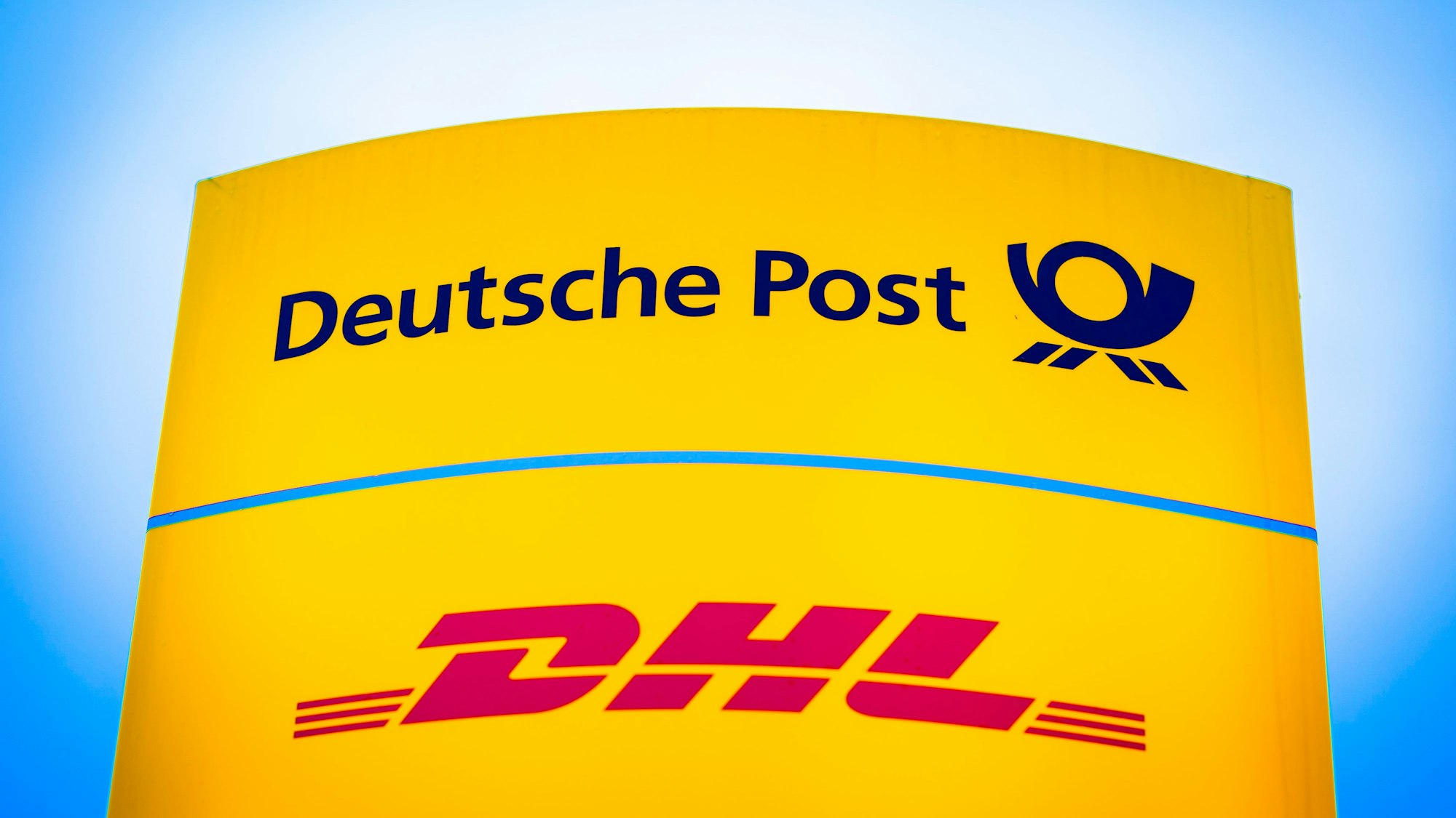 09.03.2023, Niedersachsen, Hannover: Die Logos von Deutsche Post und DHL leuchten am Morgen auf einem Schild vor einer Zustellbasis.