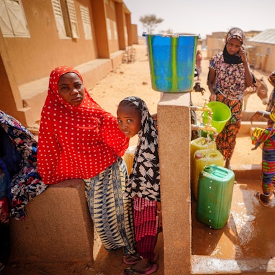 Kinder stehen an einer Wasserstelle.