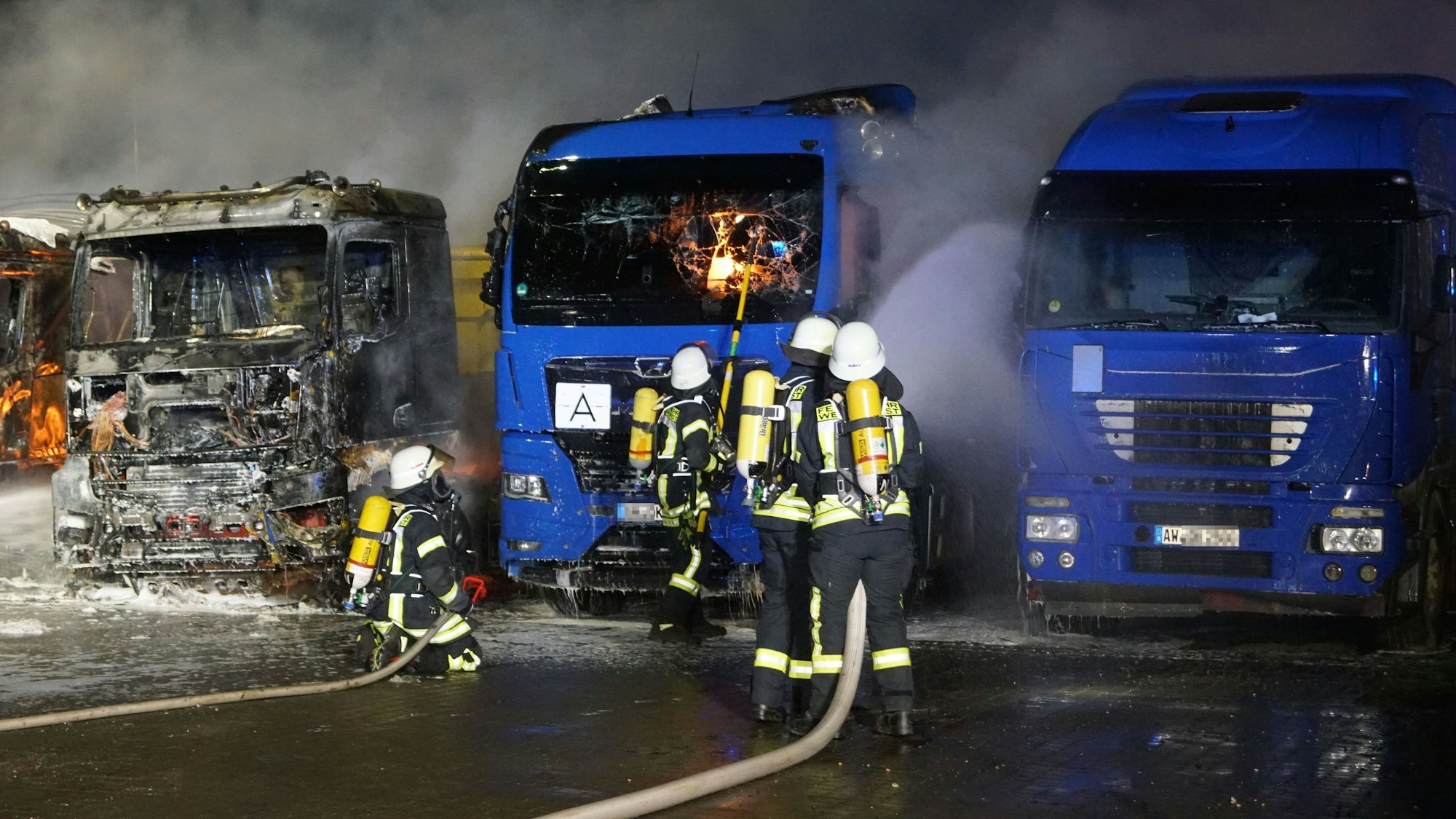Feuerwehrleute kühlen mit Wasser Lastwagen, die augenscheinlich noch intakt sind.