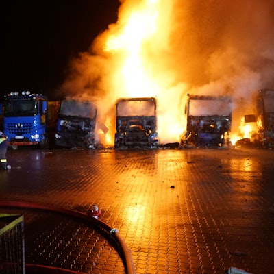 Dicht an dicht sind die Lastüge der Spedition geparkt. Man erkennt, dass drei der Laster lichterloh in Flammen anstehen. Auch an einem vierten Lkw ist Feuer zu sehen.