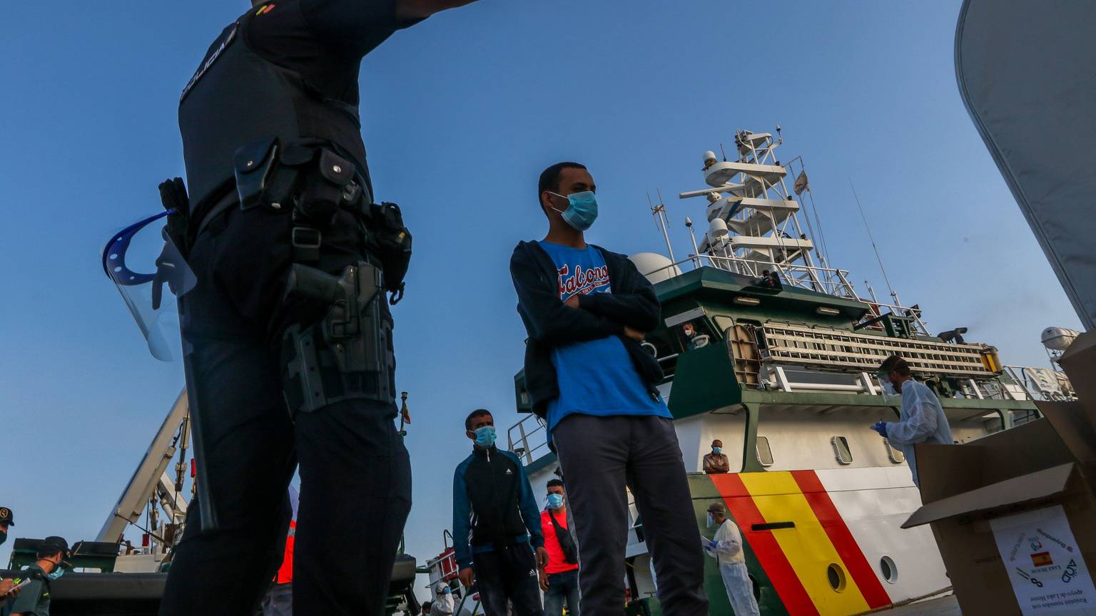 Flüchtlinge verlassen ein Schiff. Ein Mann zeigt ihnen die Richtung, in die sie gehen sollen.