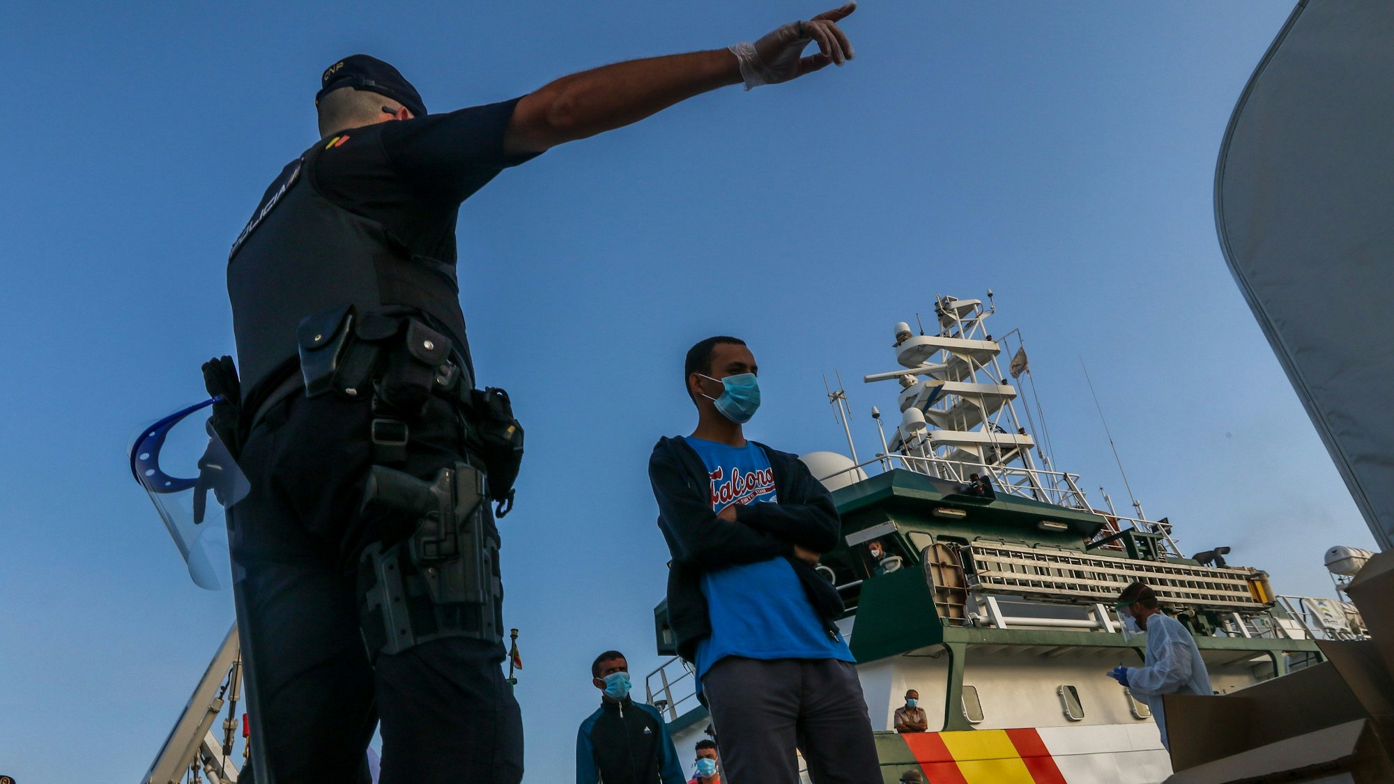 Flüchtlinge verlassen ein Schiff. Ein Mann zeigt ihnen die Richtung, in die sie gehen sollen.