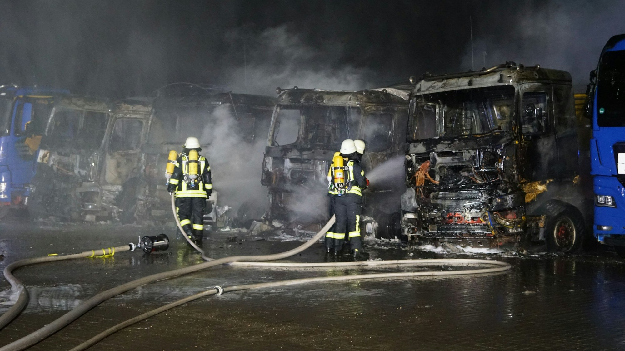 Feuerwehrleute führen Restlöscharbeiten an den zerstörten Lastwagen durch.