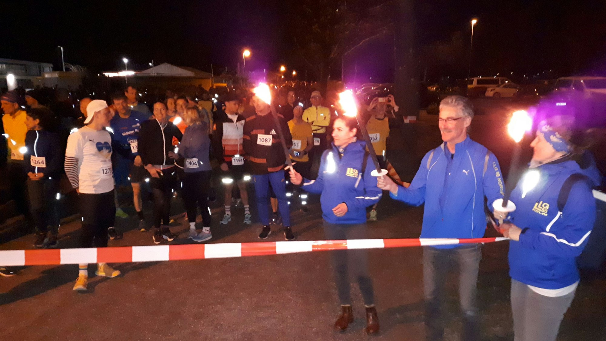 Läufer mit Fackeln stehen hinter einer Ziellinie.