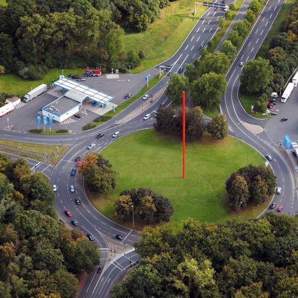 Auf einem begrünten Kreisverkehr steht eine rote Stange.