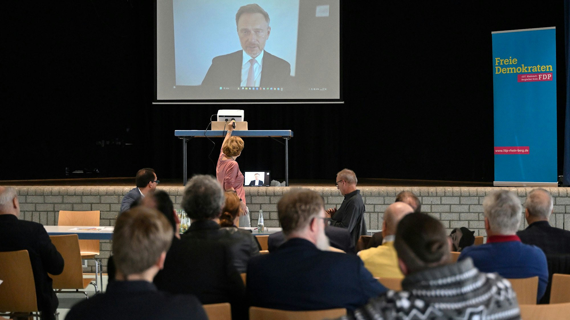 Menschen sitzen in einem Saal und schauen auf eine Leinwand, auf der im Videobild FDP-Bundesparteichef und Finanzminister Christian Lindner zu sehen ist.