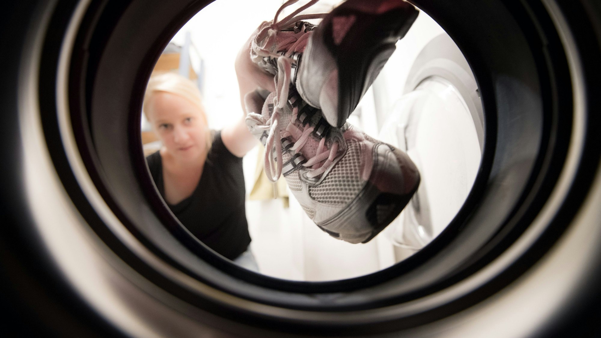 Eine Frau steckt Laufschuhe in die Waschmaschine.