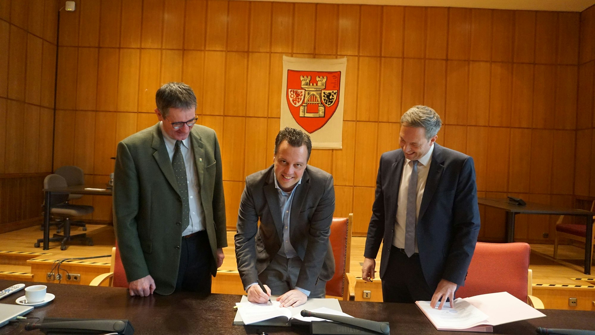 Matthias Laufer, Geschäftsführer der Friedwald GmbH (v.l.), Bürgermeister Sacha Reichelt und Forstamtsleiter Christoph Böltz unterschreiben den Kooperationsvertrag zur Anlage eines Friedwaldes im Hardtwald in Euskirchen.