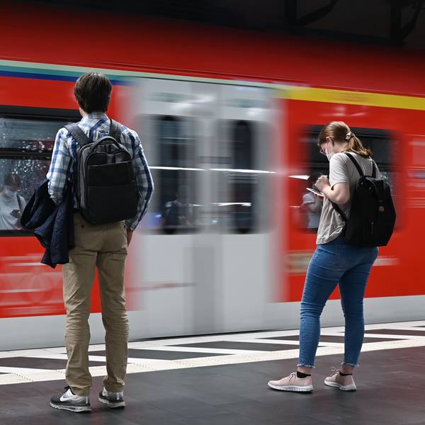 Zwei Studierende stehen am Bahnsteig, wo gerade ein Zug durchfährt.