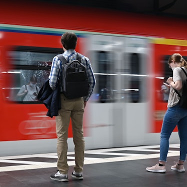 Zwei Studierende stehen am Bahnsteig, wo gerade ein Zug durchfährt.