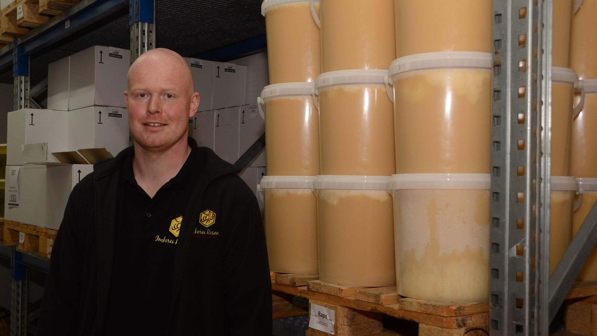 Imker Thomas Rosenau steht neben Eimern voller Honig und lächelt.