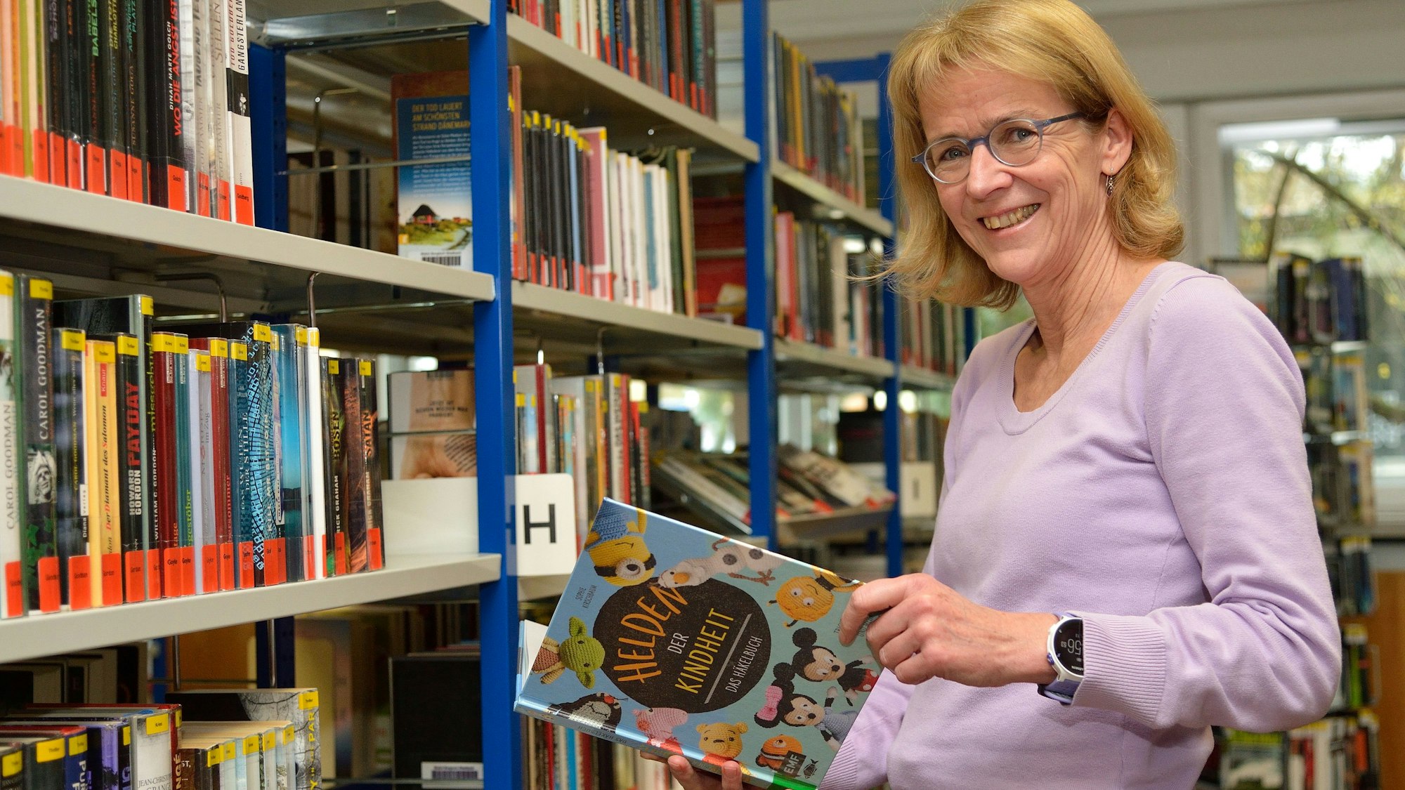 Diplom-Bibliothekarin Monika Gippert steht mit einem Buch in der Bücherei.