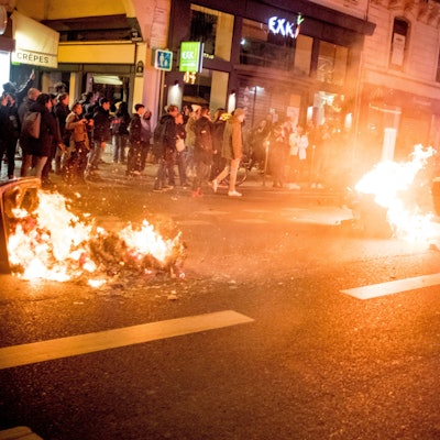 Ein Polizist fährt auf einem Motorrad an brennenden Mülltonnen in der französischen Hauptstadt Paris vorbei. In der Nacht zu Dienstag sind aufgrund der verabschiedeten Rentenreform Hunderte Menschen auf die Straßen gegangen.