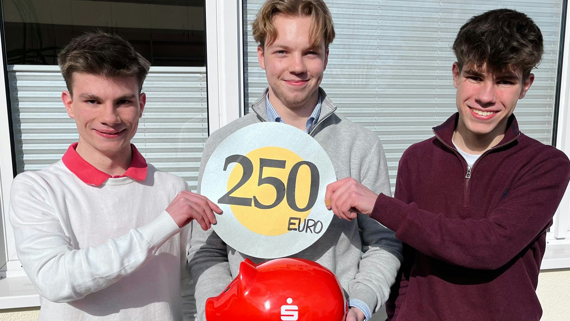 Blick auf drei jungen Männer, die in ihrer Mitte ein Sparschwein halten.