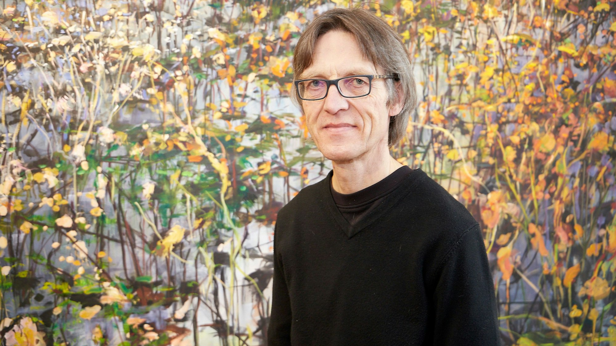 Der Künstler steht vor einem seiner Werke und blickt in die Kamera.