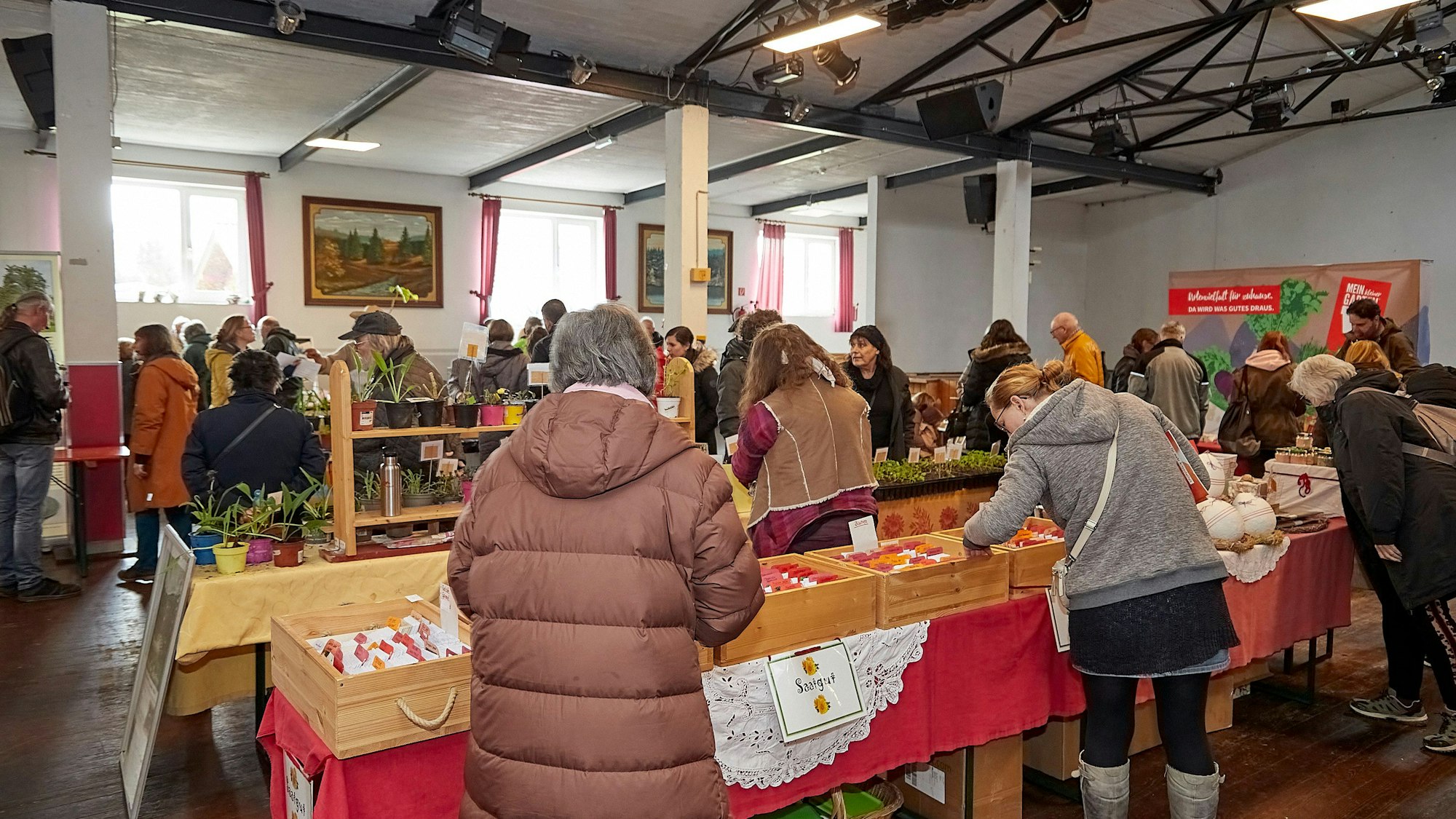 Menschen stehen in einer Halle und gucken sich Saatgut und Pflanzen an.