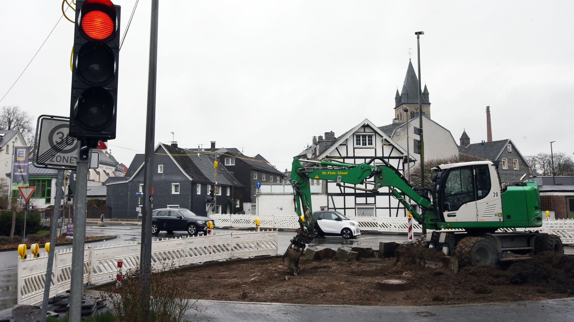 Ein Bagger arbeitet an einer Baustelle. Eine Baustellenampel zeigt Rotlicht.