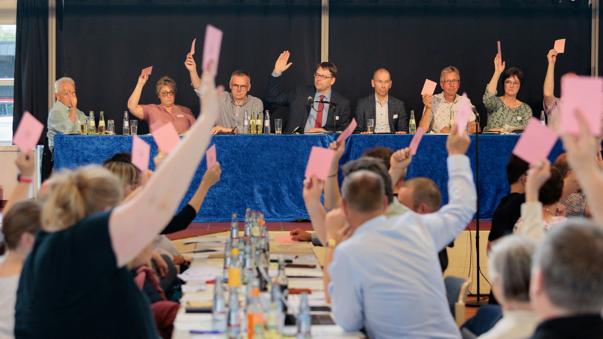 Die Presbyter bei der Sommersynode 2022. Personen halten bei einer Wahl Stimmzettel in die Luft.