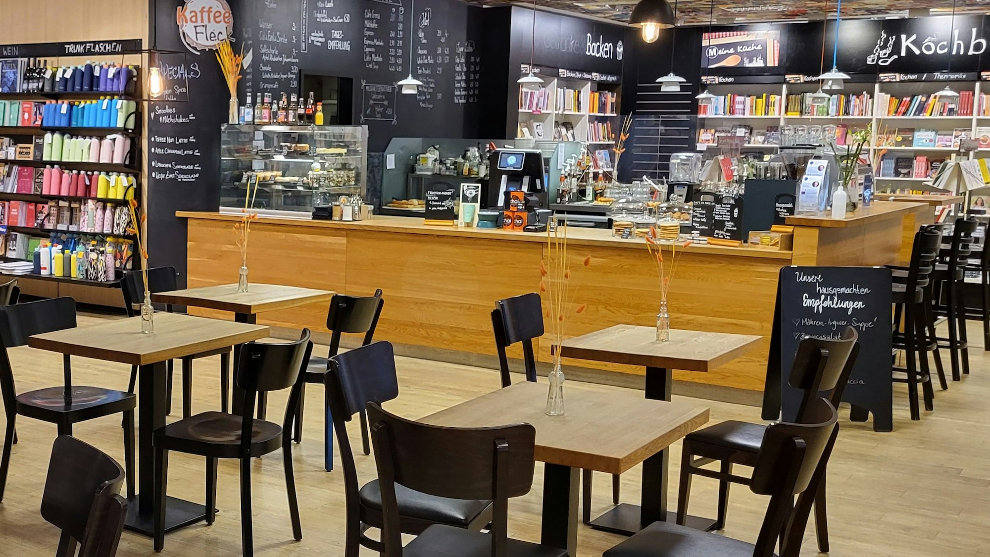 Ein paar Holztische, eine Kuchentheke und rundherum Bücherregale: So sieht es im Kaffee Fleck in der Mayersche-Buchhandlung aus.