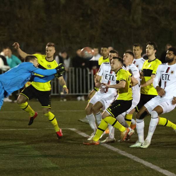 Ein Torwart in blauem Trikot faustet einen Ball zurück. Spieler in gelb-schwarzen Trikots und weißen Trickots nehmen ihn im Spiel wieder an.